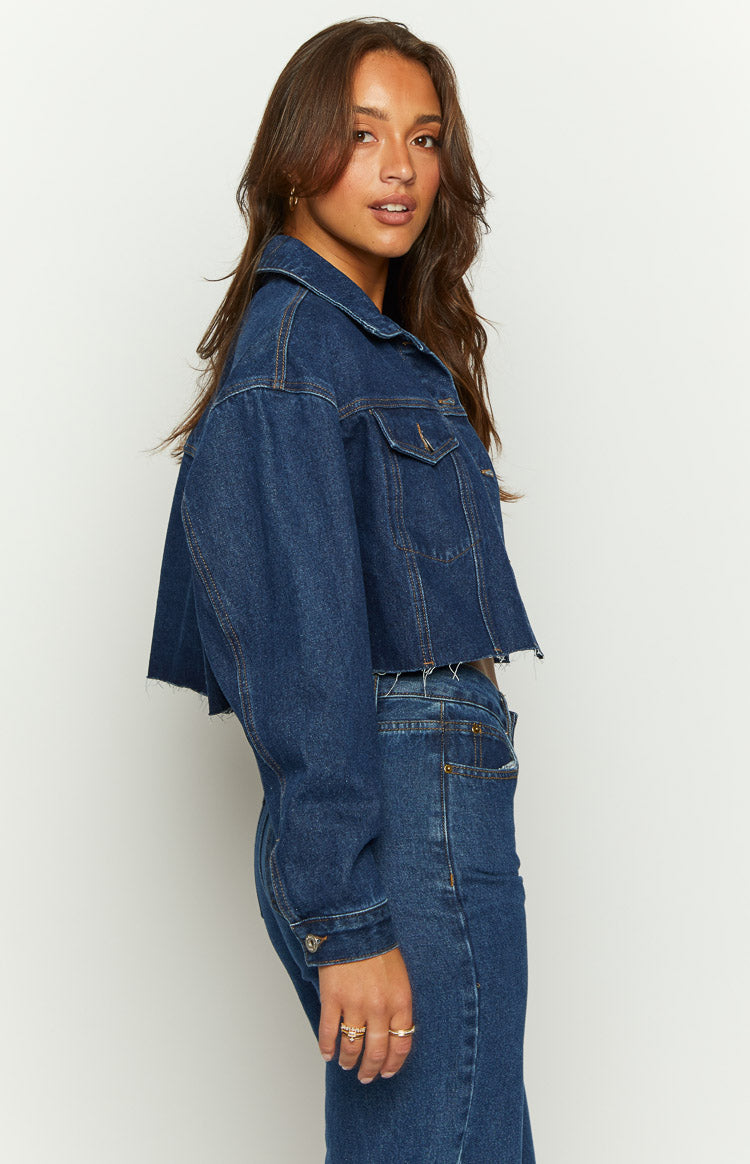 Side view of a dark wash denim cropped jacket with a raw hem and relaxed fit