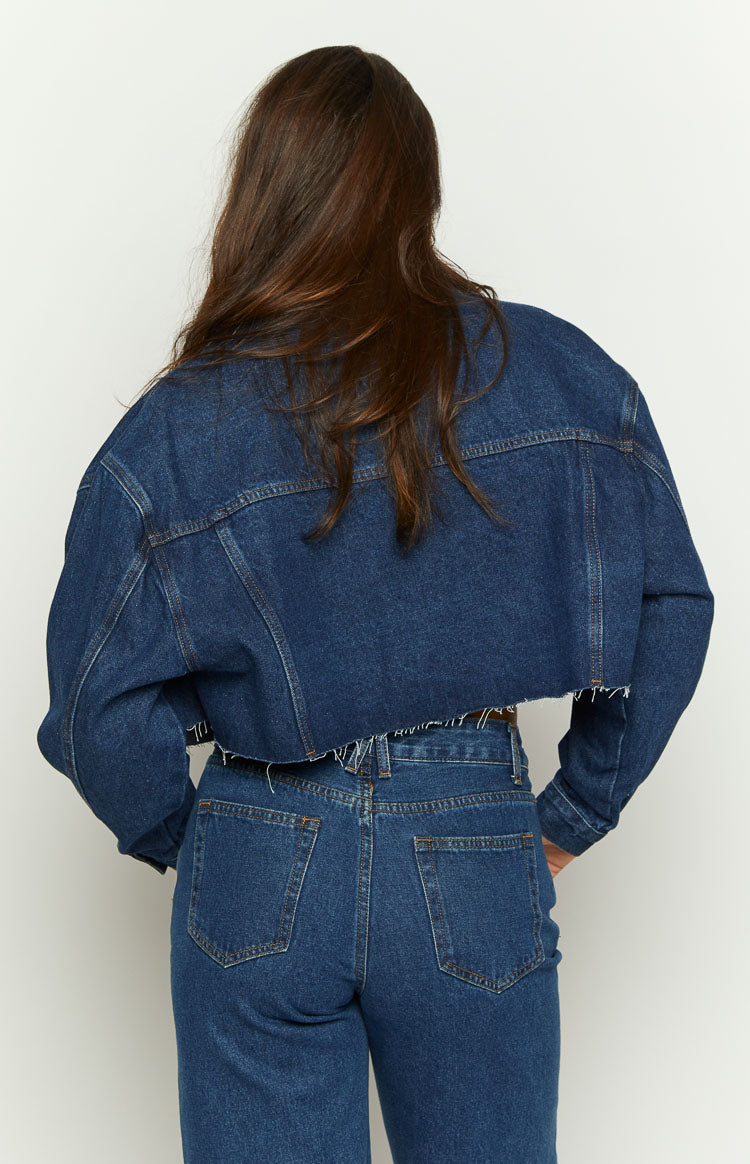 Rear view of a dark wash denim cropped jacket with a raw frayed hemline and back yoke stitching
