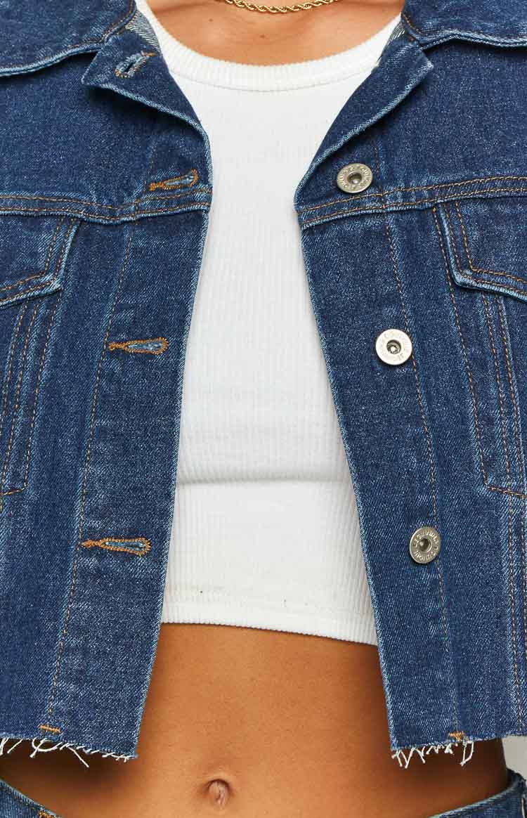 Close-up of the dark wash denim jacket showing silver buttons, chest pockets, and frayed hem