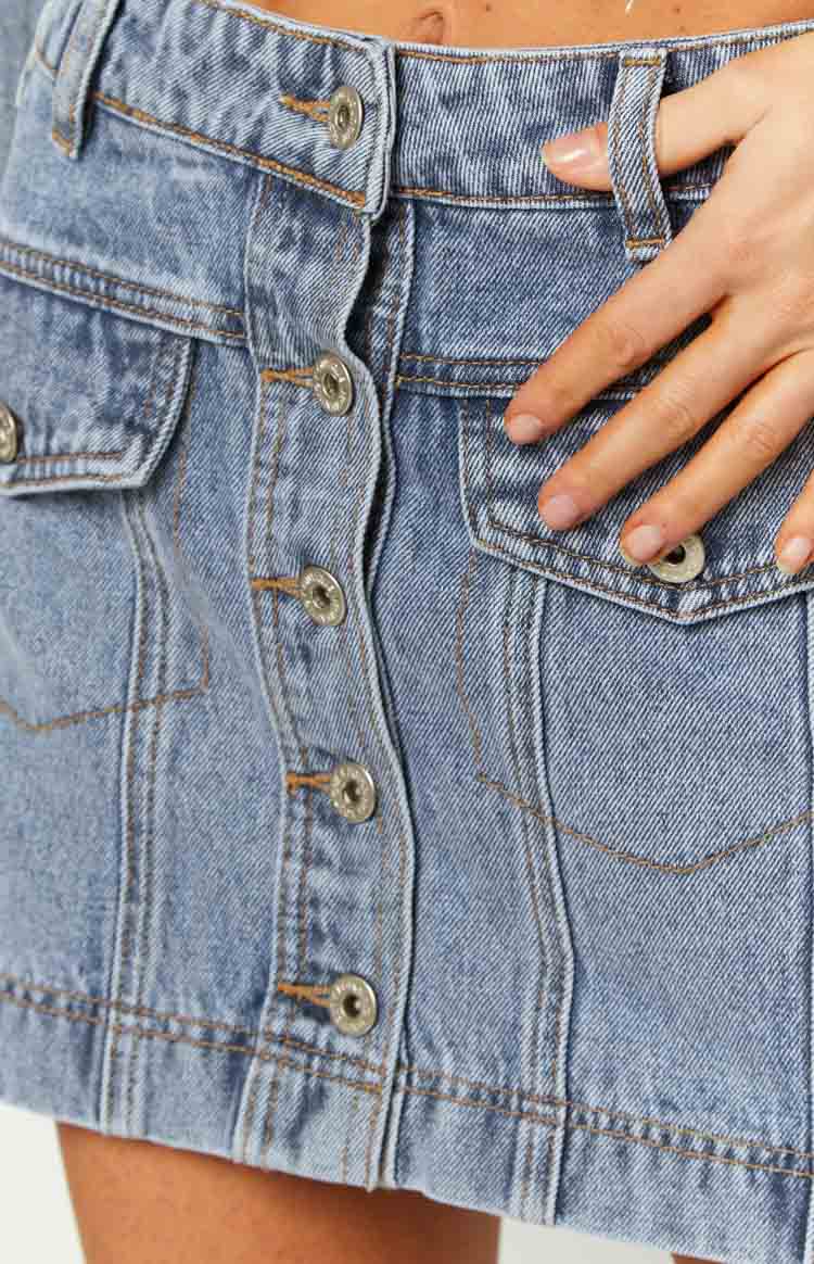 Close-up of the button-front closure and flap cargo pockets on a mid-wash denim mini skirt