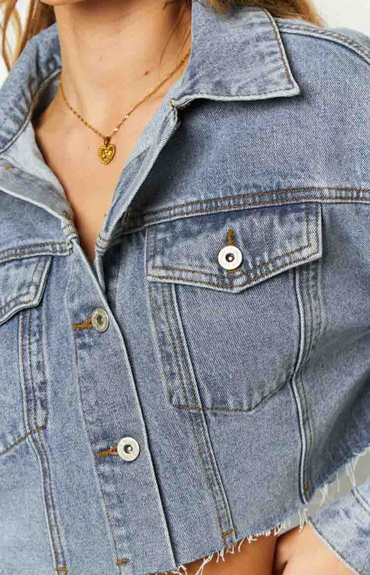 Close-up of the mid wash denim jacket showing the collared neckline, button-flap chest pockets, and silver front buttons