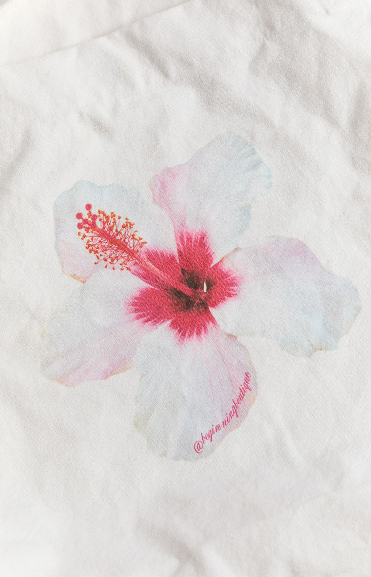 Close-up of the white hibiscus print with pink center and red stamen on the tote bag, showing the brand logo