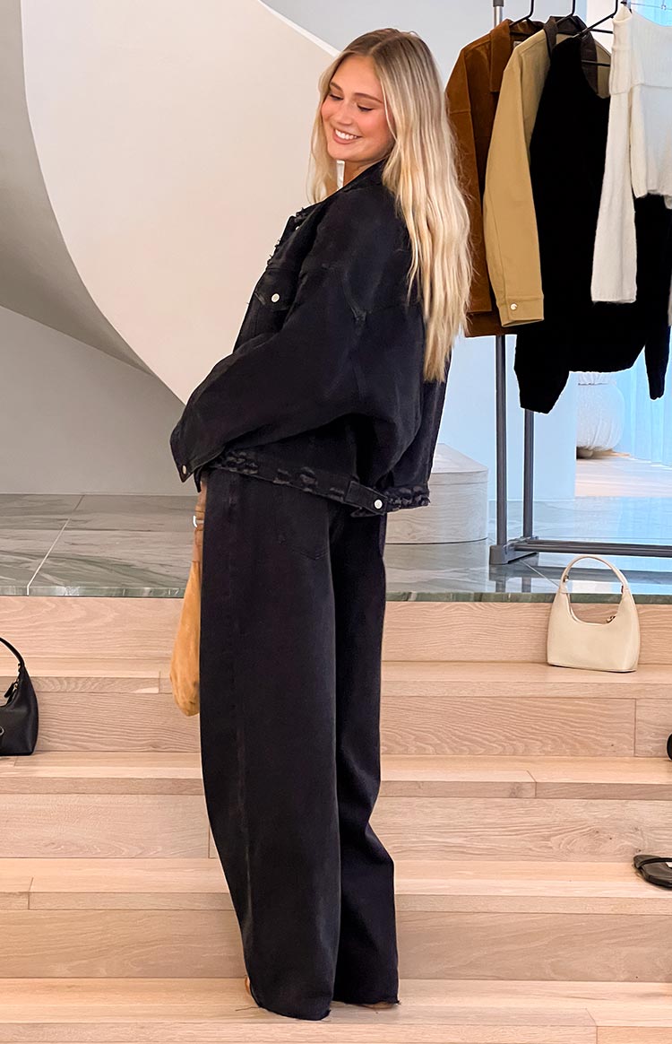 Side view of a black oversized denim jacket with a distressed frayed hem