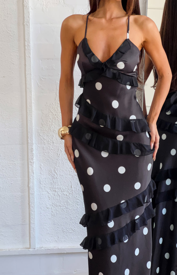 Close-up of the black polka dot maxi dress showing the V-neck, spaghetti straps, and diagonal ruffle tiers