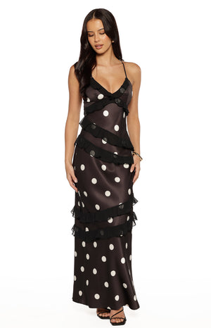 Model wearing a black polka dot maxi dress with ruffled layers and spaghetti straps for a wedding guest