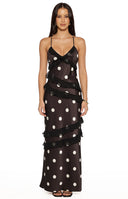 Model wearing a black polka dot maxi dress with ruffled layers and spaghetti straps for a wedding guest
