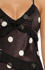 Close-up of the V-neckline, sheer black ruffles, and side zipper on a black satin polka dot maxi dress