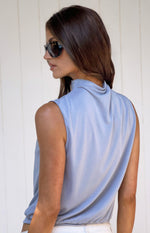 Side view of a dusty blue sleeveless top with a draped high neckline and gathered hem