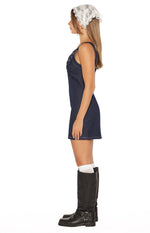 Side view of a dark wash denim mini dress with white contrast stitching and front buckle details