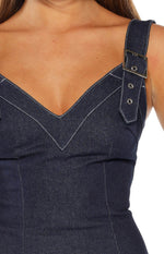 Close-up of the dark wash denim mini dress showing the silver buckle strap and white contrast V-neck stitching