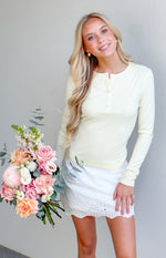 Pale yellow ribbed knit long sleeve top with a round henley neckline and three button placket