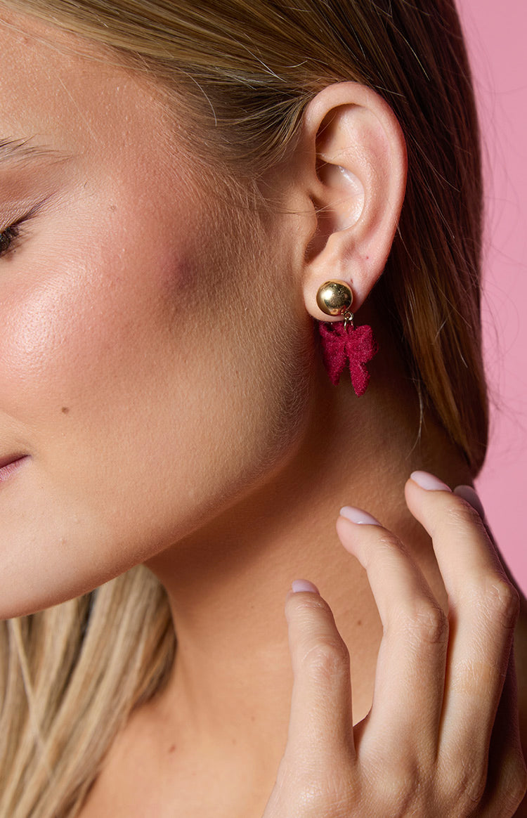 Close-up of a gold stud earring with a textured red bow hanging from it