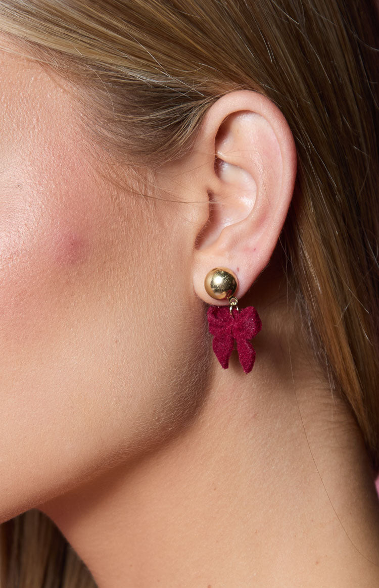 Close-up of a small red velvet bow earring dangling from a gold ball stud