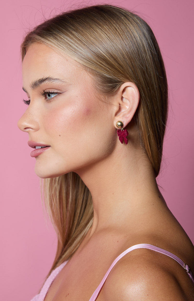 Close-up side view of a deep red fabric bow earring with a gold ball stud