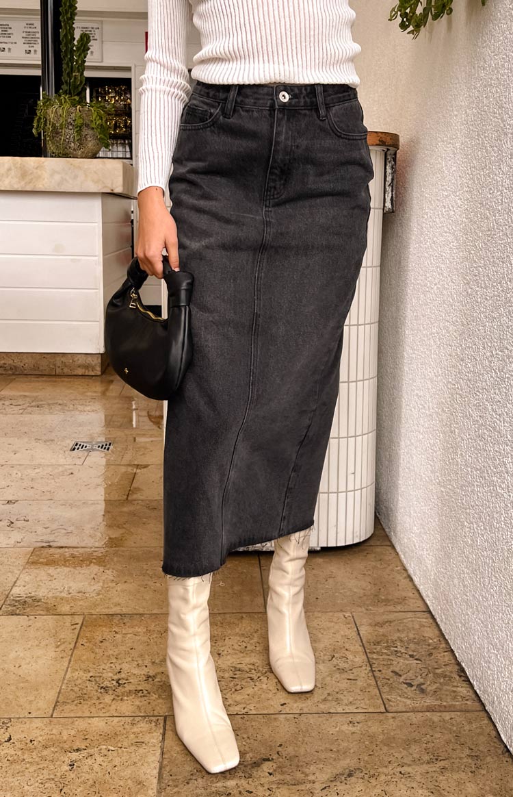 Washed black denim midi skirt with a front button closure, vertical seam detail, and raw frayed hem