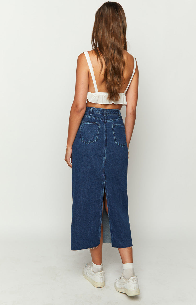 Back view of a dark denim midi skirt with two back pockets, a center slit, and a frayed raw hem