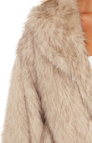 An extreme close-up of a shaggy long-haired faux fur coat in a light tan or beige color.