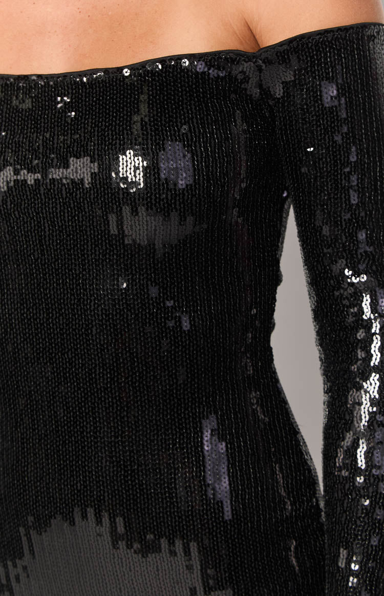 Close-up of the shimmering black sequin fabric, off-shoulder neckline, and fitted long sleeve of the mini dress