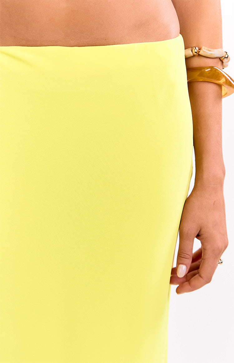 Close-up of the smooth, bright yellow fabric of the maxi skirt, showing the flat waistband and fitted hip