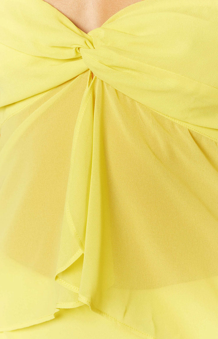 Close-up of the twisted knot detail at the bust of the yellow strapless top, showing the sheer, layered fabric