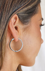 Side view of a large silver hoop earring covered in sparkling diamantes, worn on an ear