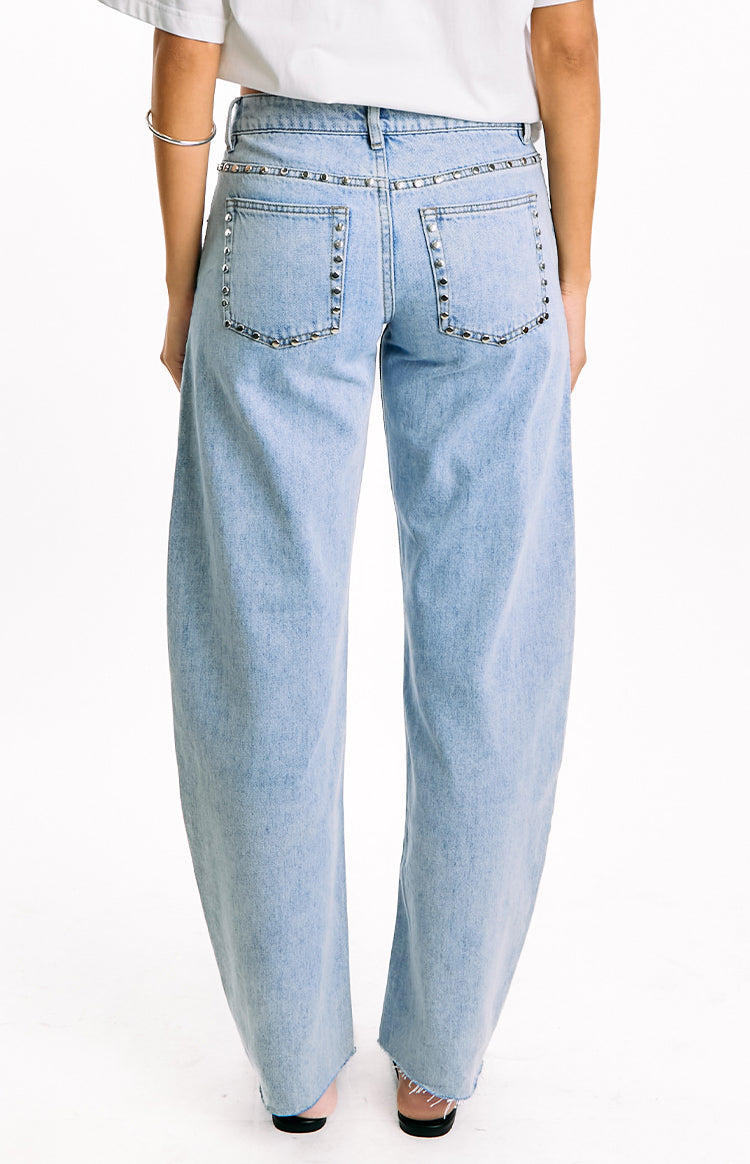 Rear view of light wash low rise jeans with silver studs along the waistband and outlining the back pockets