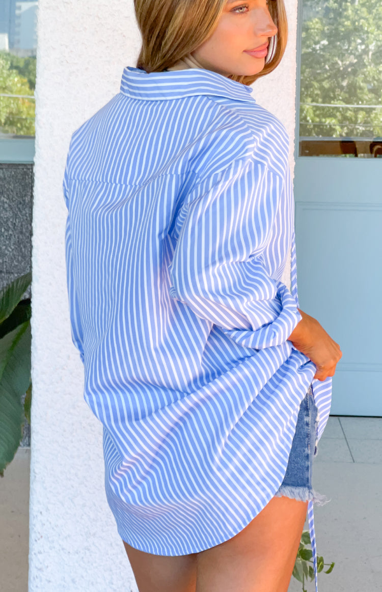 Side view of a blue pinstripe shirt dress with an oversized fit and rolled long sleeves