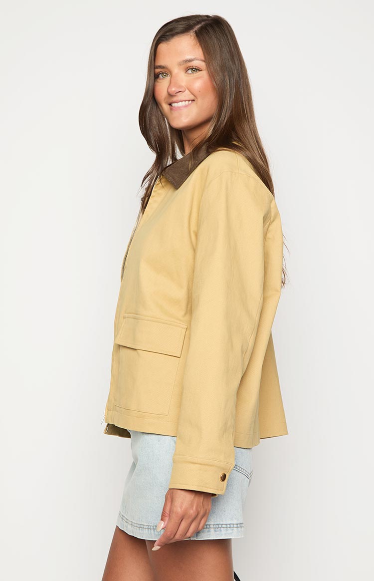 Side view of a cream canvas jacket with a brown contrast collar, flap pocket, and button cuff