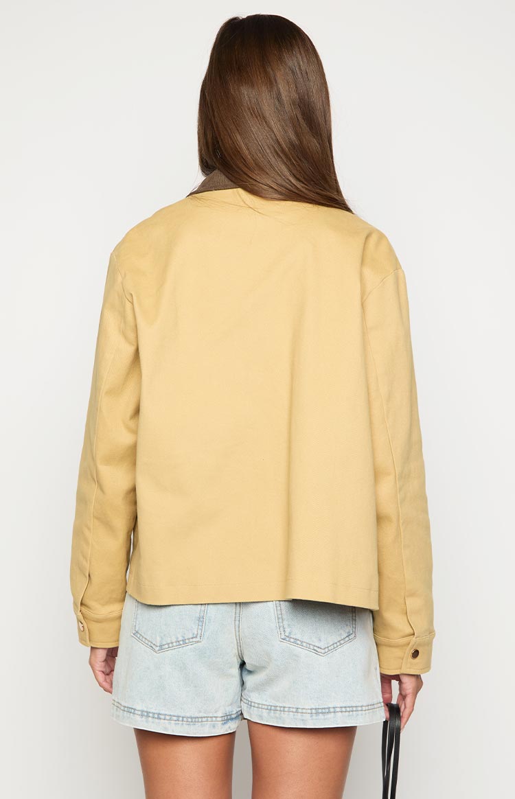 Rear view of a cream canvas jacket with a brown contrast collar and buttoned cuffs