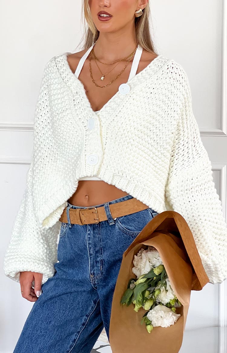 Front view of a white chunky knit cardigan with large buttons and a cropped fit