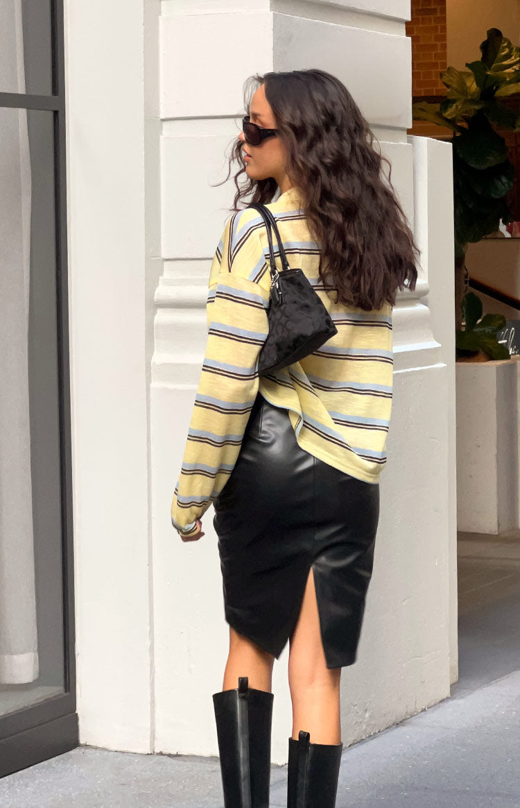 Side view of a fitted black PU midi skirt, showing the sleek faux leather texture and a high back slit