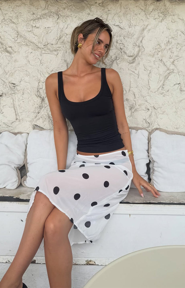 Seated view of the white sheer midi skirt with black polka dots, revealing the transparent fabric and relaxed fit