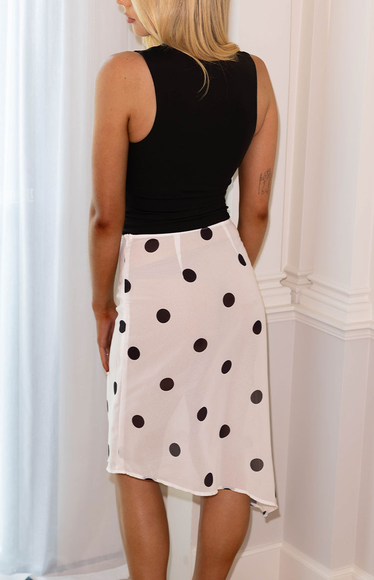 Rear view of the white sheer midi skirt with black polka dots and a flowing asymmetrical hemline