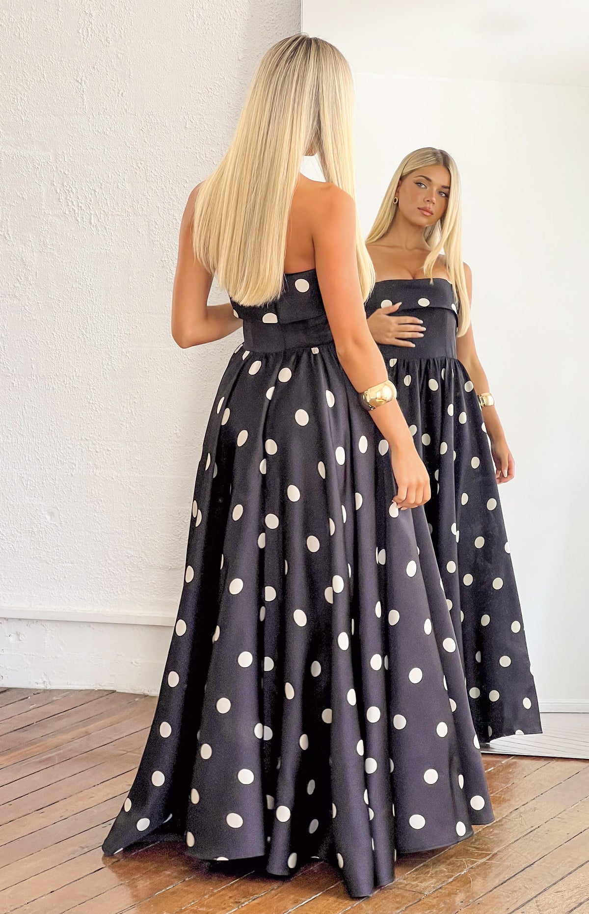Rear view of a black polka dot strapless satin maxi dress with a fitted bodice and full flowing skirt