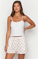 Girl wearing white tank top and cherry print pajama pants holding christmas mug.