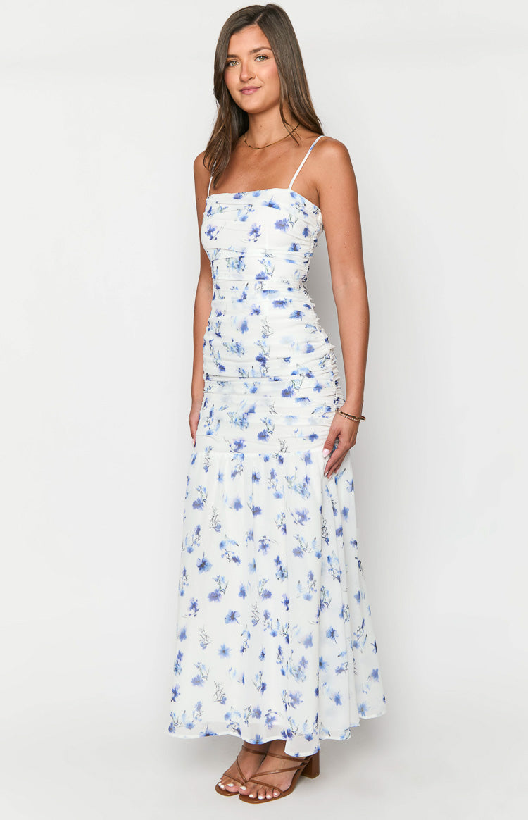 Side view of a white floral maxi dress with a ruched bodice and a flowy skirt with blue floral print