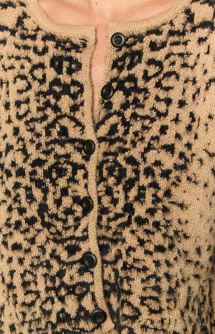 Close-up of the round neckline and black button-front of a tan knitted cardigan with textured leopard print