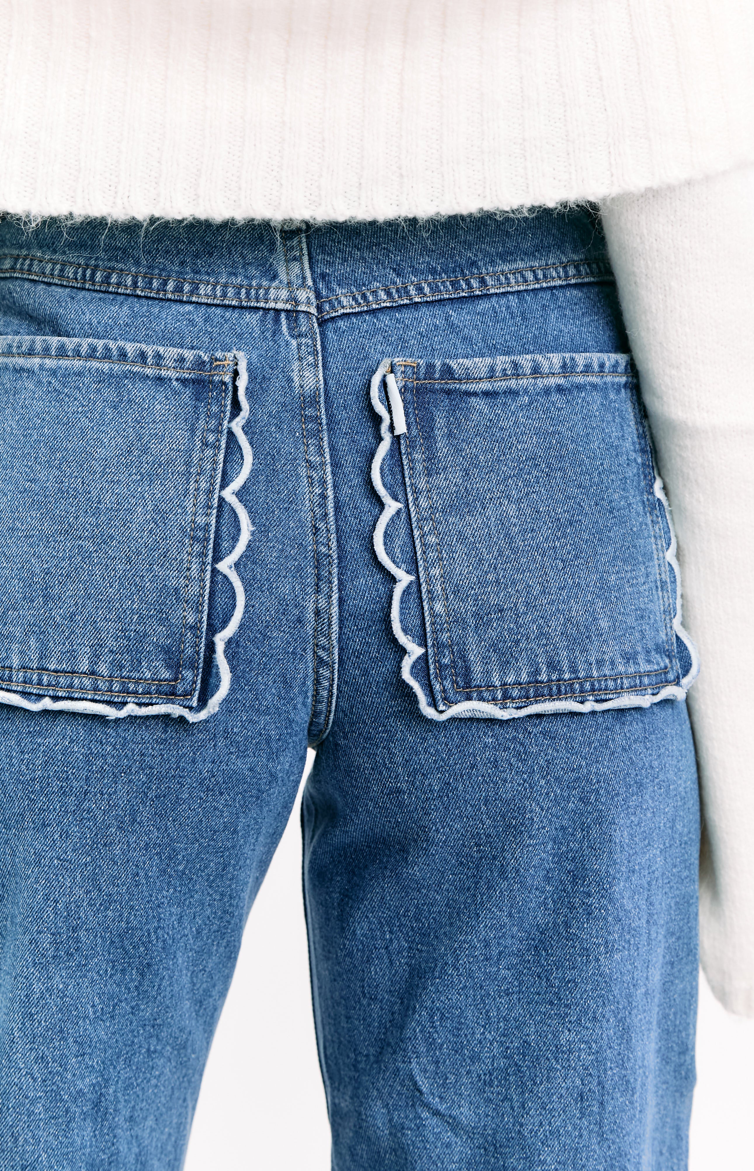 Close-up rear view of mid-wash denim jeans featuring white scalloped edges on the two back pockets