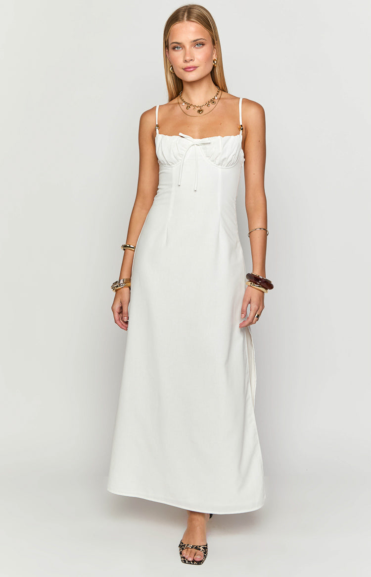 White maxi dress with a sweetheart neckline, ruched bust, front tie detail, and thin spaghetti straps with gold hardware