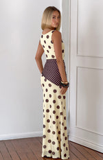 Side view of a yellow maxi dress with brown polka dots and a contrasting diagonal brown panel with white polka dots at the wa
