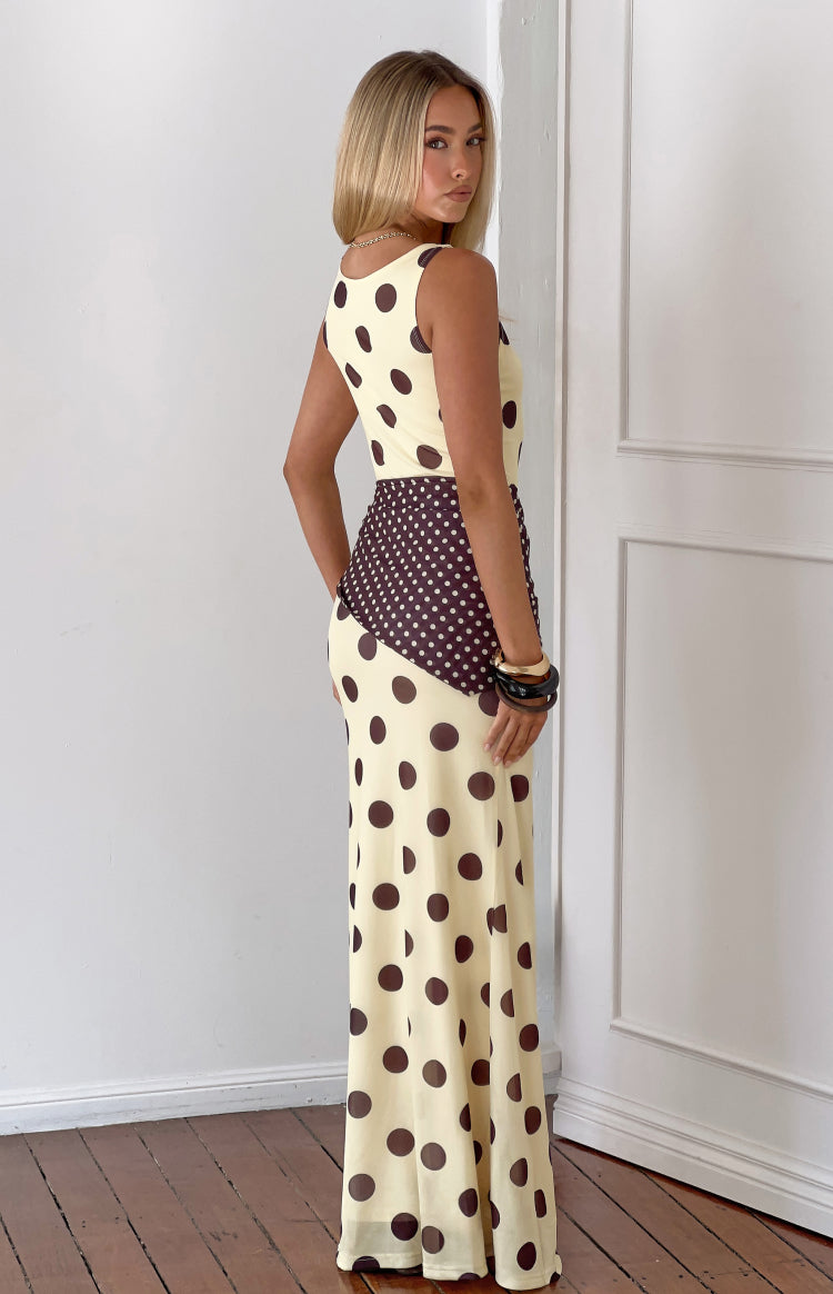Side view of a yellow maxi dress with brown polka dots and a contrasting diagonal brown panel with white polka dots at the wa