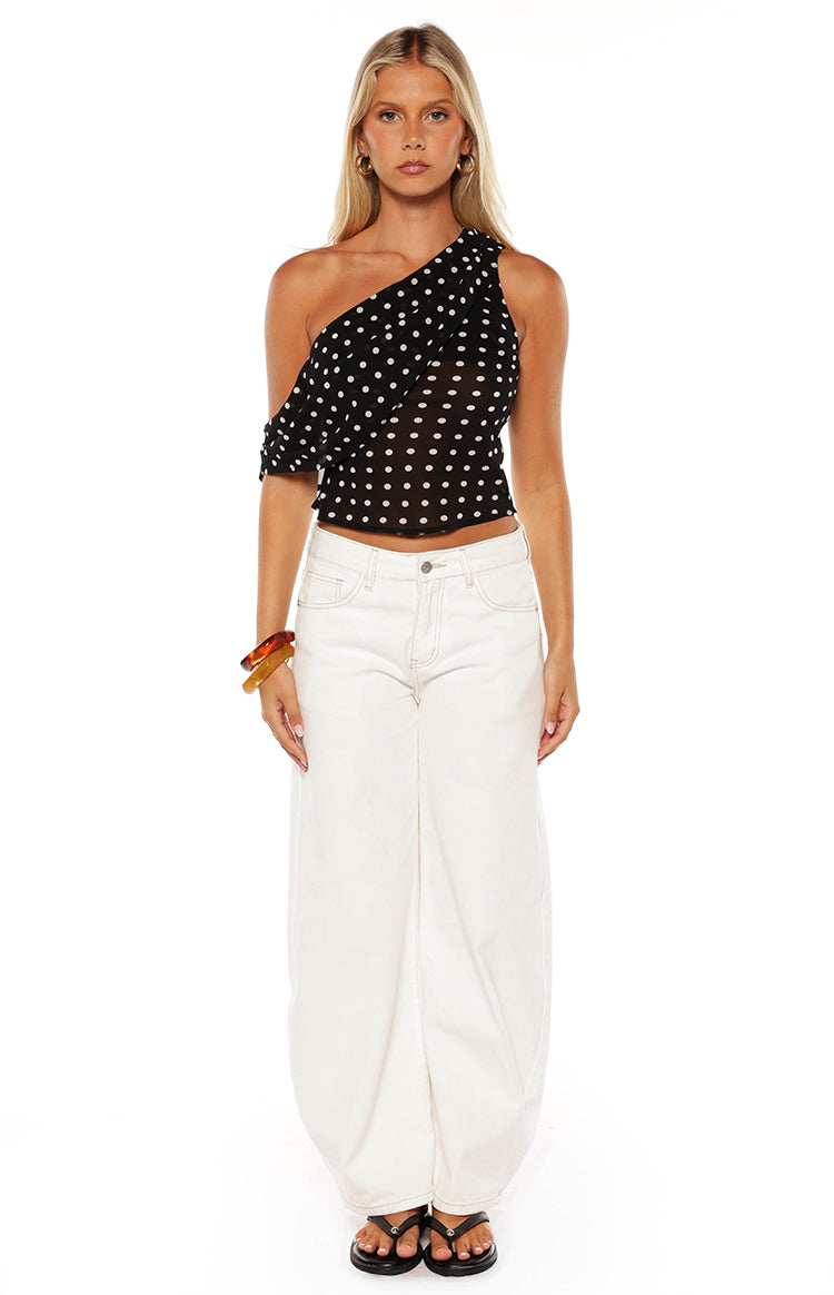 Black polka dot one-shoulder top with a draped ruffle sleeve and cropped hem