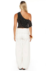 Rear view of a black polka dot off-shoulder top with a single strap and ruffled detail