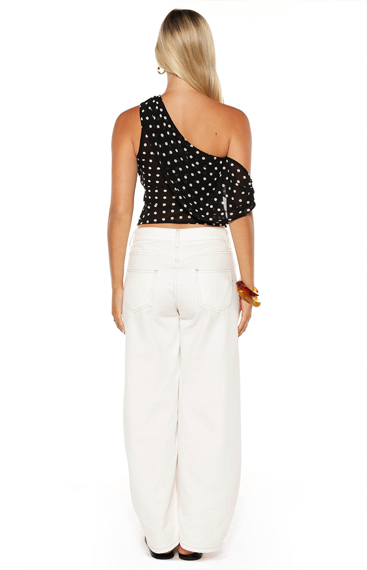 Rear view of a black polka dot off-shoulder top with a single strap and ruffled detail