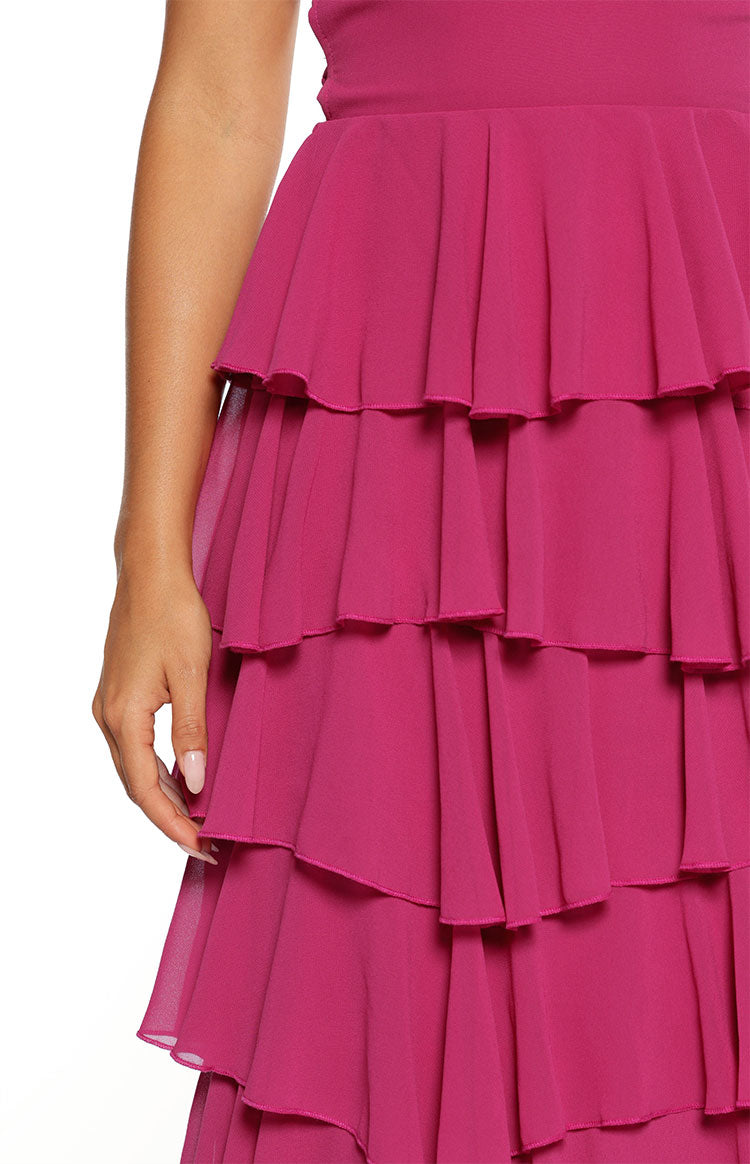 A close-up view focuses on the tiered skirt of a vibrant fuchsia maxi dress. The skirt is made of multiple layers of sheer giving the volume flowing ruffles appearance set closely together.