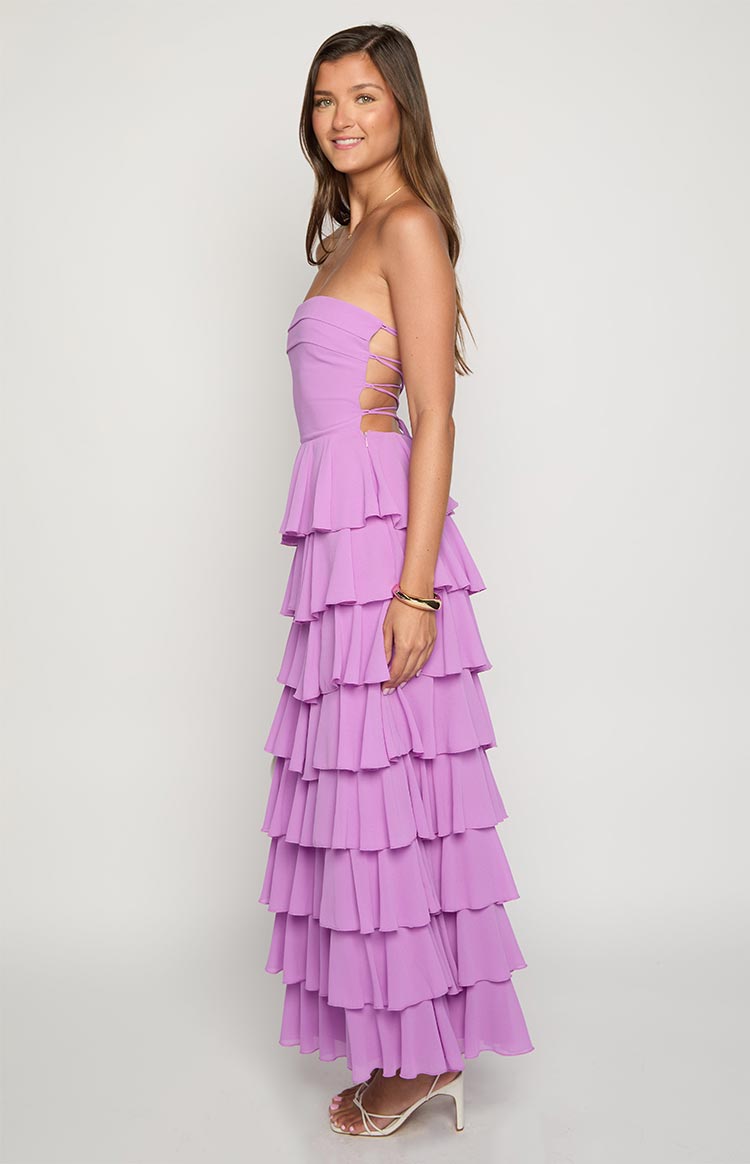 Side view of a magenta strapless maxi dress with lace-up side cutouts and a tiered ruffle skirt