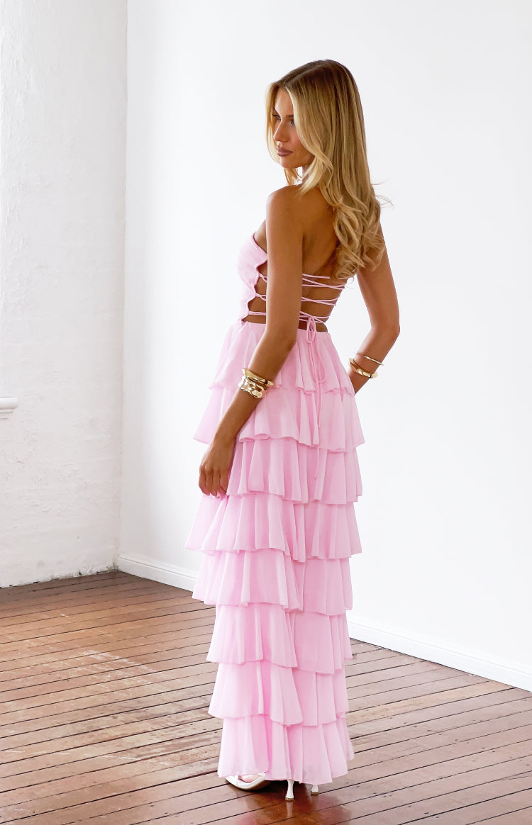Side view of a pink strapless maxi dress with lace-up side cutouts and a tiered ruffle skirt
