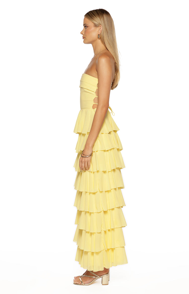 Side view of a yellow strapless maxi dress with side cutouts and a tiered ruffle skirt
