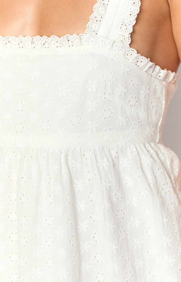 Close-up of white broderie anglaise mini dress with floral eyelet pattern, scalloped lace trim, and gathered waist