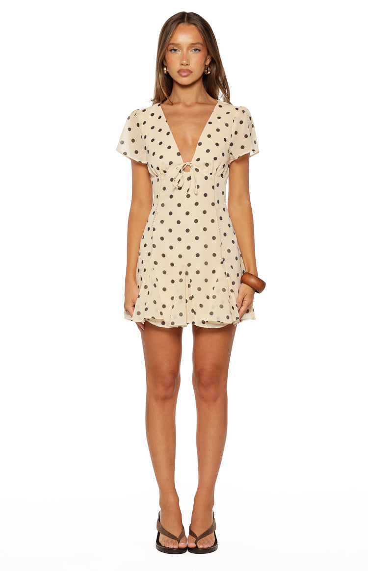 Cream polka dot mini dress with a deep V-neck, tie-front bust, short flutter sleeves, and a ruffled mini hem
